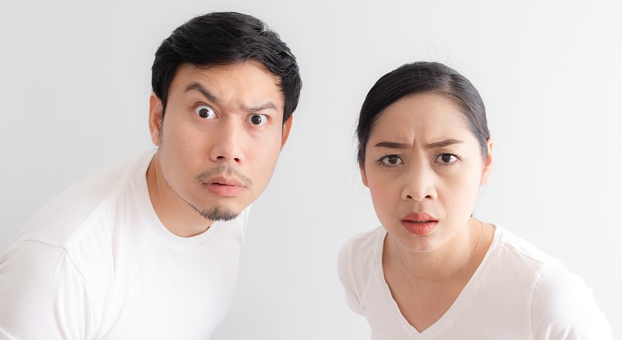 Funny face of Asian lovers couple in doubt at an unbelievable thing that they are looking at